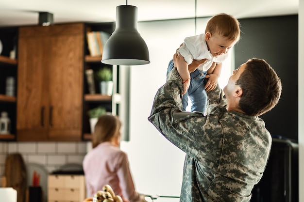 Gelukkig jongetje dat plezier heeft met zijn militaire vader thuis Moeder is op de achtergrond