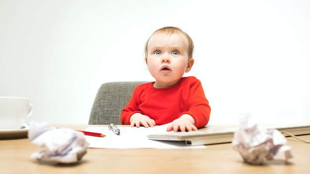 Gelukkig kind babymeisje zit met toetsenbord van moderne computer of laptop geïsoleerd op een witte studio.