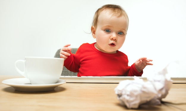 Gelukkig kind babymeisje zit met toetsenbord van moderne computer of laptop in wit