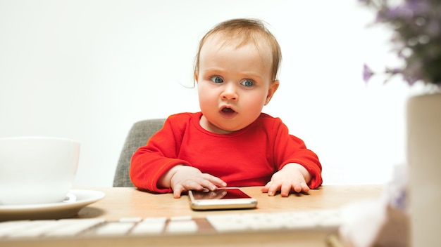 Gelukkig kind babymeisje zit met toetsenbord van moderne computer of laptop in wit