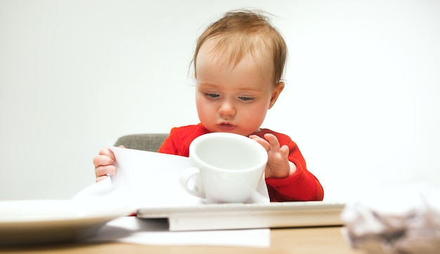 Gelukkig kind babymeisje zit met toetsenbord van moderne computer of laptop in witte studio