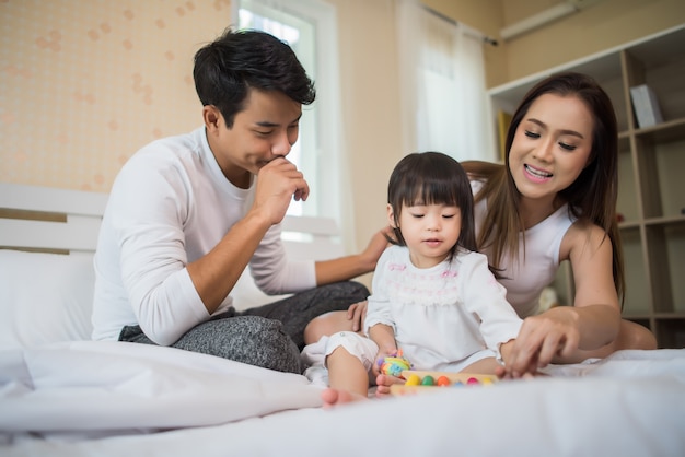 Gelukkig kind met ouders die in het bed thuis spelen