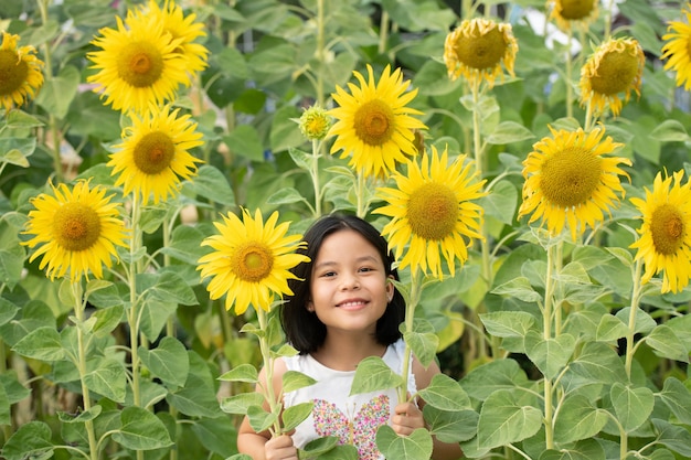 Gelukkig klein aziatisch meisje met plezier tussen bloeiende zonnebloemen onder de zachte stralen van de zon.