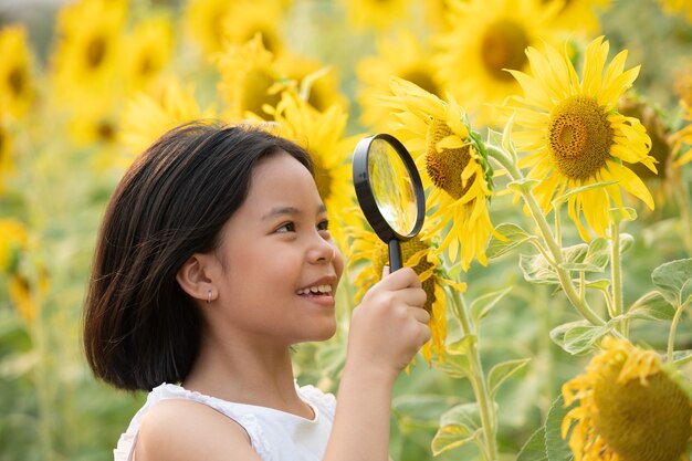 gelukkig klein Aziatisch meisje met plezier tussen bloeiende zonnebloemen onder de zachte stralen van de zon.