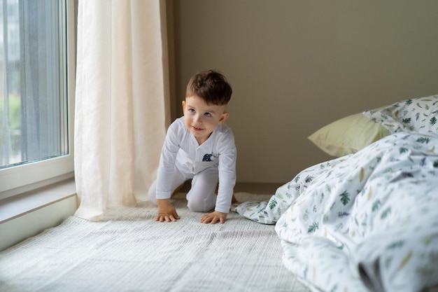 Gelukkig klein kindjongen in pyjama, in bed in de slaapkamer met speelgoed, speelt, slaapt. Prachtig babybed. Slaap overdag voor kinderen. Zacht licht.