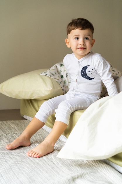 Gelukkig klein kindjongen in pyjama, in bed in de slaapkamer met speelgoed, speelt, slaapt. prachtig babybed. slaap overdag voor kinderen. zacht licht.