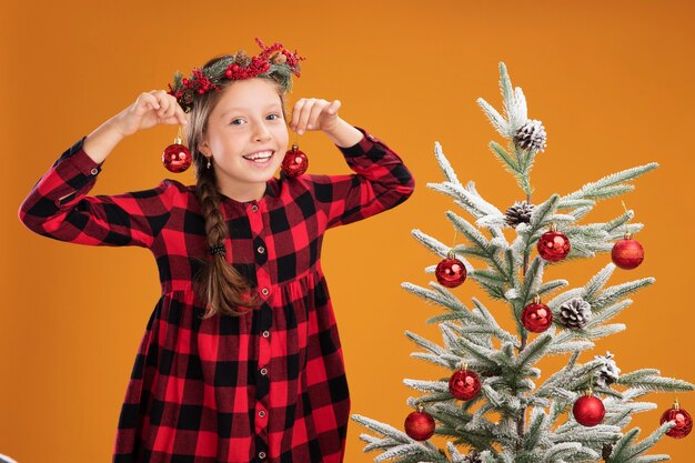 Gelukkig klein meisje dat de kroon van Kerstmis in ingecheckte overhemd draagt met kerstballen