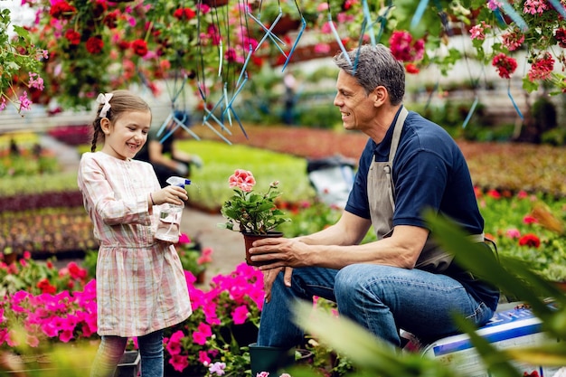 Gelukkig klein meisje dat plezier heeft met haar vader terwijl ze een spuitfles gebruikt en potbloemen water geeft op de plantenkwekerij