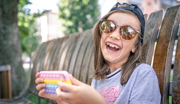 Gelukkig klein meisje in zonnebril met een smartphone in een trendy hoesje knalt het.