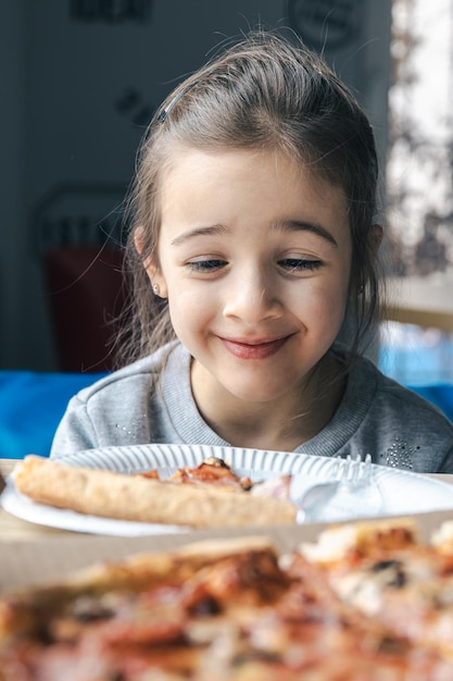 Gelukkig klein meisje kijkt met eetlust naar pizza