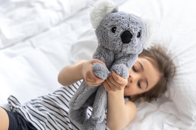 Gelukkig klein meisje met zacht stuk speelgoed koala in bed