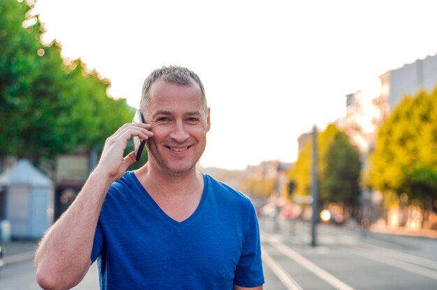 Gelukkig lachend veertig jaar oude Kaukasische toerist man praten op een mobiele telefoon buiten.