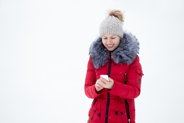 Gelukkig lachend vrouw in rode winterjas met mobiele telefoon, buitenshuis tegen de sneeuw