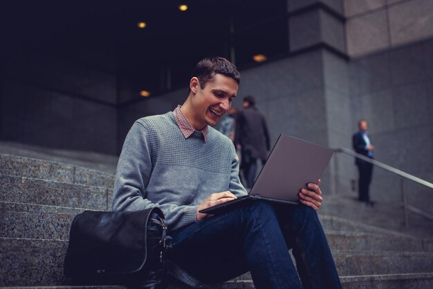 Gelukkig lachende jonge man met laptop in een centrum van de stad.