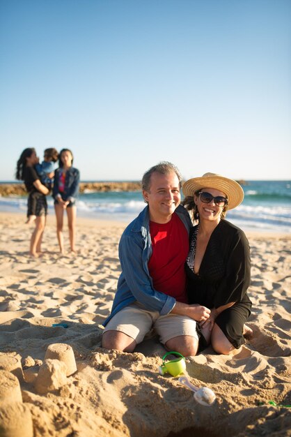 Gelukkig lachende man en vrouw op het strand. Man en vrouw zitten aan het zand, knuffelen, kijken naar de camera