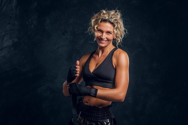 Gelukkig lachende vrouwelijke bokser poseert voor fotograaf in donkere fotostudio.