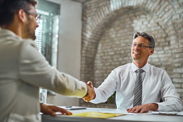 Gelukkig manager handenschudden met een kandidaat na succesvol sollicitatiegesprek op kantoor