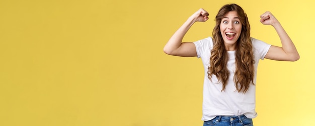 Gratis foto gelukkig meisje dat zich als een winnaar voelt en een opgewekte, vrolijke jonge vrouw triomfeert, hand opsteekt, vuist pompt cele op