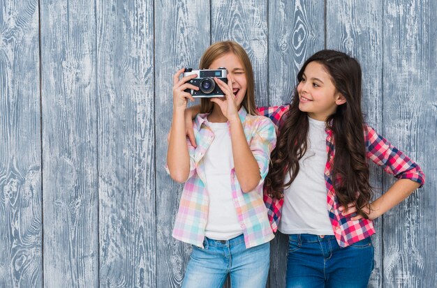 Gelukkig meisje die haar vriend bekijken die door uitstekende camera kijken die zich tegen houten muur bevinden