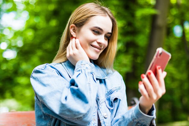 Gelukkig meisje met behulp van een telefoon in een stadspark zittend op een bankje