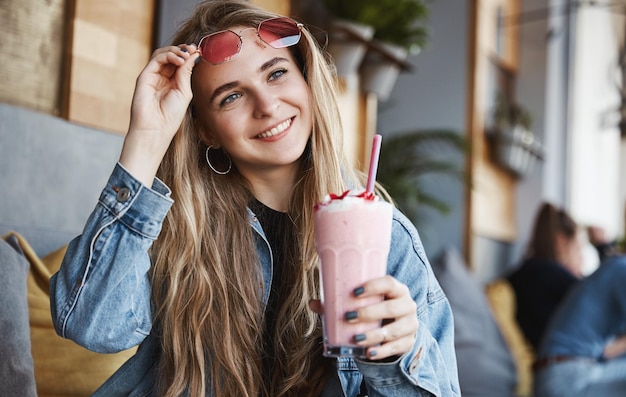 Gelukkig meisje opstijgen zonnebril en smoothie drinken in café ter