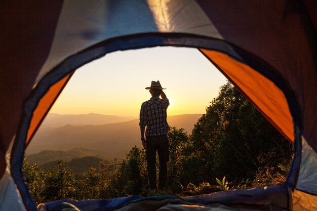 Gelukkig mensverblijf dichtbij tent rond bergen onder zonsondergang lichte hemel genietend van de vrije tijd en de vrijheid.