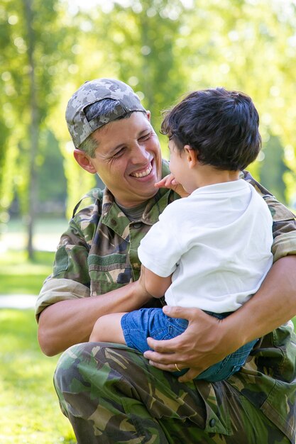 Gelukkig militaire vader zoontje in armen houden, jongen buiten knuffelen na terugkeer van zendingsreis. Familiereünie of het concept van thuiskomst