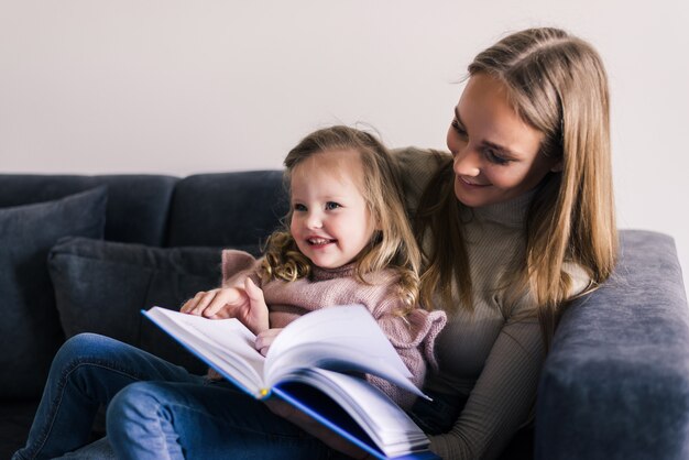 Gelukkig moeder en dochtertje leesboek, zittend op een comfortabele bank in de woonkamer