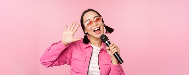 Gelukkig mooi Aziatisch meisje zingen met microfoon met behulp van microfoon genieten van karaoke poseren tegen roze studio achtergrond