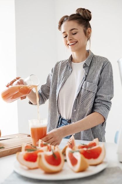 Gelukkig mooi meisje gieten grapefruit detox smoothie in glas glimlachend over witte muur. Gezonde voeding.