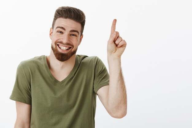 Gelukkig opgetogen en zorgeloze aantrekkelijke volwassen man met baard lachen vreugdevol met geweldige tijd kijken opgetogen en vreugdevol naar boven gericht of nummer één tonen over witte muur