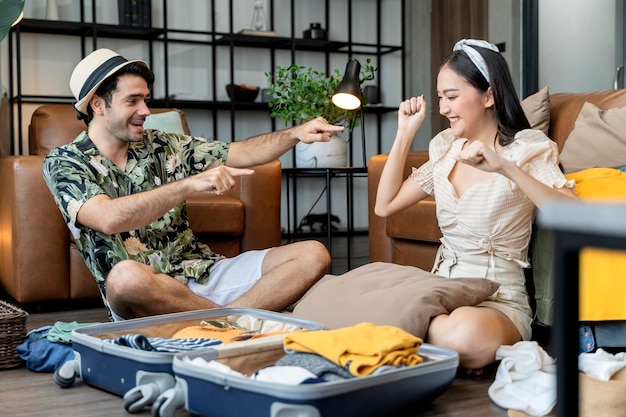 Gelukkig paar aziatische en blanke trouwen minnaar dragen casual doek genieten van het verpakken van doek en reisspullen bagage op de vloer in woonkamer minnaar paar zingen en grappige dans samen thuis