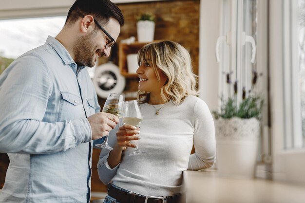 Gelukkig paar dat elkaar aankijkt tijdens het roosteren met wijn in de keuken