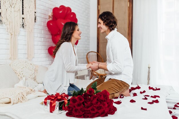 Gelukkig paar hand in hand, boeket rode rozen en geschenkdoos op het bed