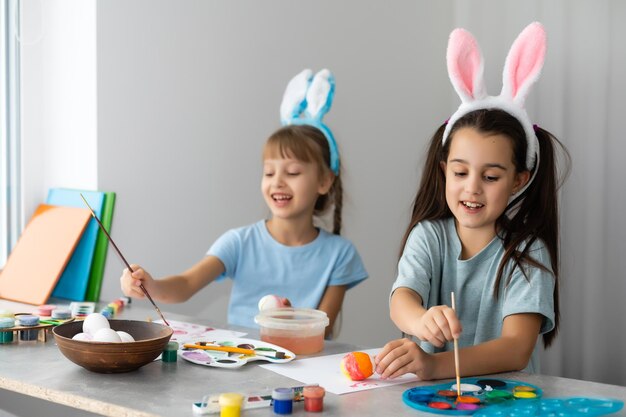 Gelukkig pasen. twee zussen paaseieren schilderen. gelukkige familiekinderen die zich voorbereiden op pasen. schattig klein kindmeisje met konijnenoren op paasdag.