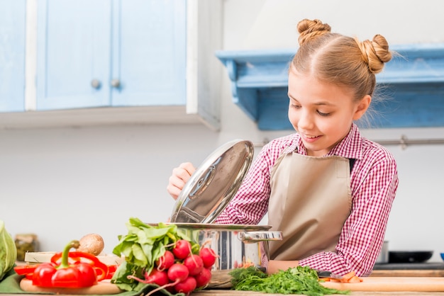 Gelukkig portret van een meisje die roestvrij staal kokende pot op lijst in de keuken bekijken