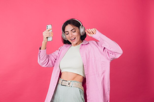 Gelukkig positieve vrouw in koptelefoon op roze rode muur