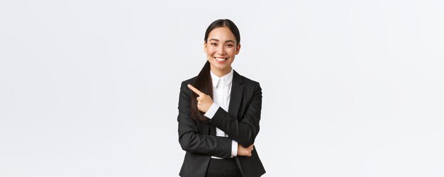 Gelukkig professionele Aziatische vrouwelijke manager zakenvrouw in pak met aankondiging glimlachend en wijzende vinger links naar product of project banner staande witte achtergrond
