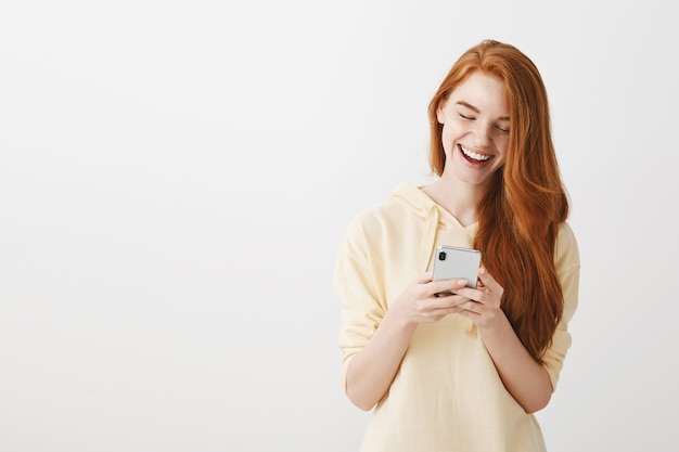 Gelukkig roodharige meisje sms-vriend, smartphone met glimlach kijken
