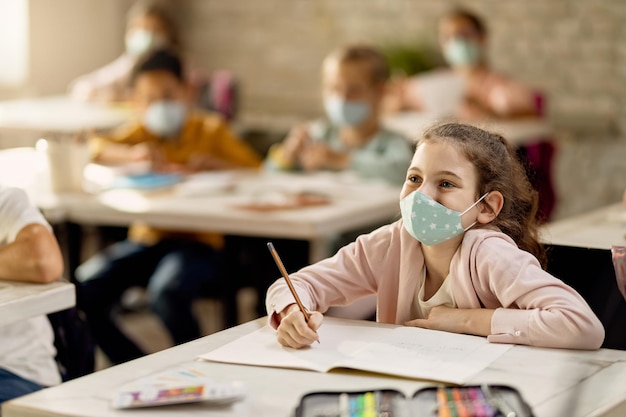 Gelukkig schoolmeisje dat een gezichtsmasker draagt tijdens een lezing in de klas