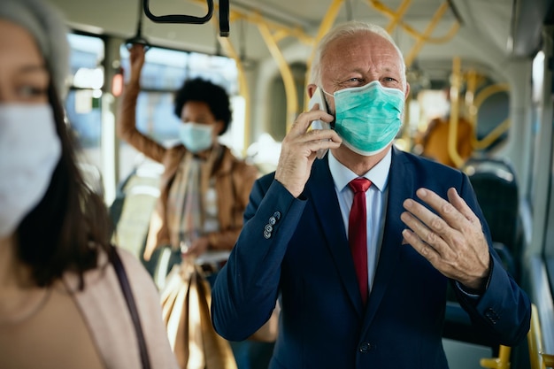 Gelukkig senior zakenman met gezichtsmasker praten aan de telefoon in een openbaar vervoer