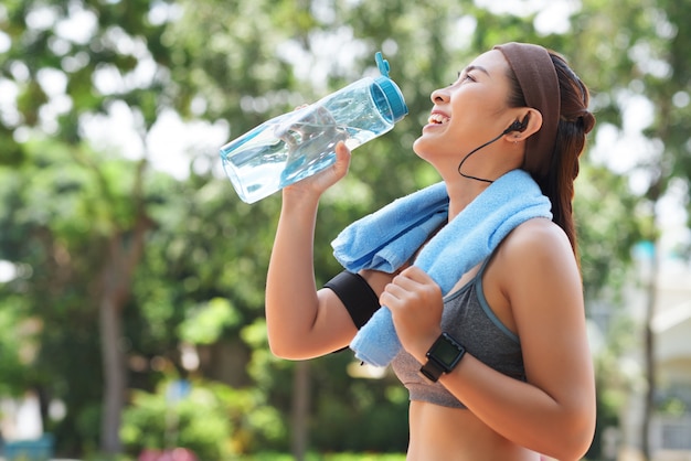 Gelukkig sportvrouw drinkwater in park