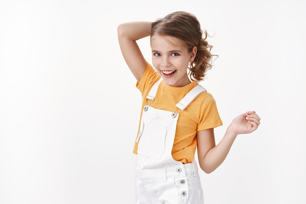 Gelukkig stijlvol schattig klein kindmeisje, blond haar kammen om met de speeltuin van vrienden te spelen, breed lachend genieten van koele zomervakanties, camera zorgeloos lachen, tuinbroek dragen