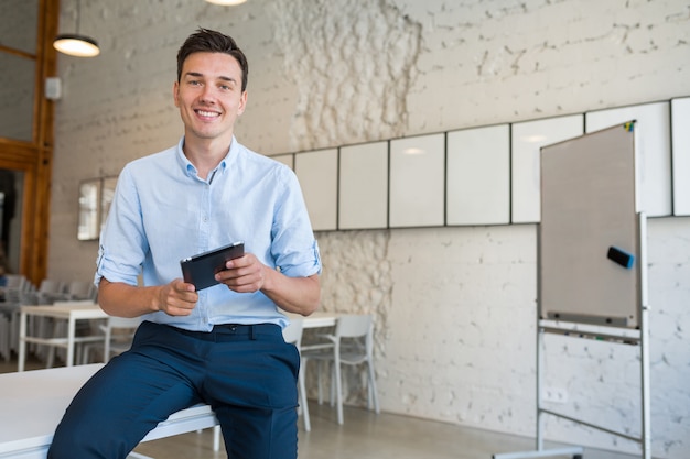 Gelukkig stijlvolle lachende jongeman in co-working office, opstarten freelancer bedrijf met behulp van tablet,