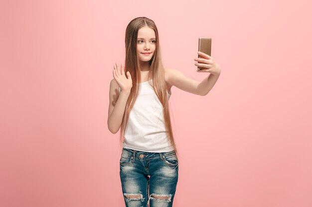 Gelukkig tiener meisje permanent, glimlachend op roze, selfie foto maken via de mobiele telefoon. Menselijke emoties, gezichtsuitdrukking concept