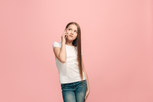 Gelukkig tiener meisje staan, glimlachend met mobiele telefoon over trendy roze studio