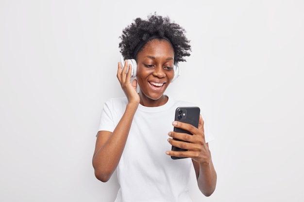 Gelukkig tienermeisje met Afro-kapsel kiest nummer uit afspeellijst met mobiele telefoon