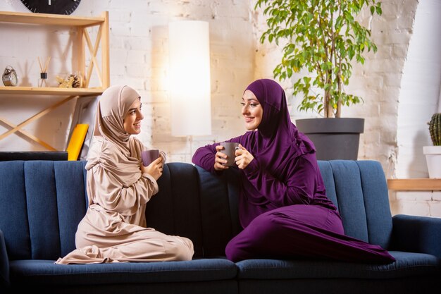 Gelukkig twee moslimvrouwen thuis tijdens de les, studeren in de buurt van computer, online onderwijs