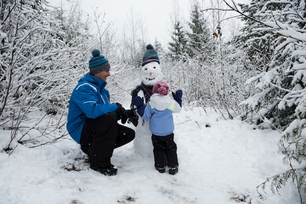 Gelukkig vader kijken dochter sneeuwpop maken