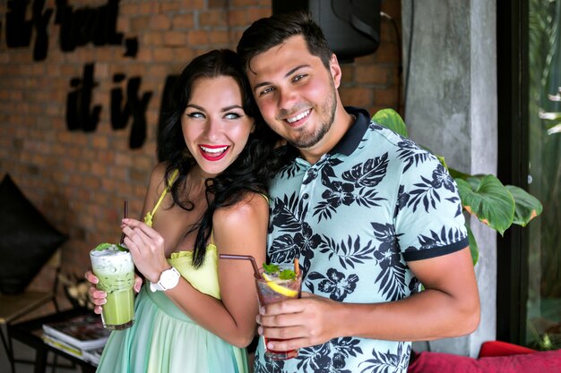 Gelukkig vrij jong koppel genieten van hun lekkere zoete cocktail in tropische bar, kleur bijpassende trendy kleding, zomervakantie stemming. Perfecte romantische date.